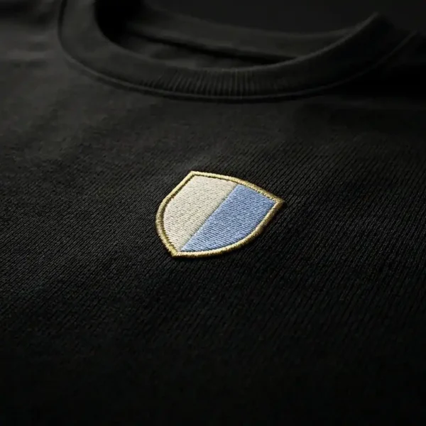 close up of embroidered shield logo on black oversized t-shirt premium cotton fabric